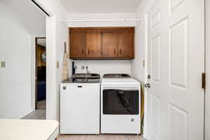 Laundry room with cabinet space, washer and clothes dryer, baseboards, and light wood-style flooring