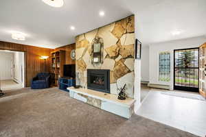 Unfurnished living room featuring wooden walls, a stone fireplace, carpet flooring, and baseboard heating