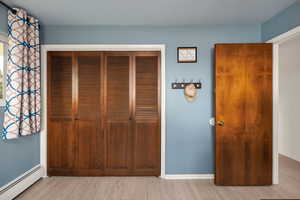 Unfurnished bedroom with light wood-type flooring, a closet, a baseboard heating unit, and baseboards