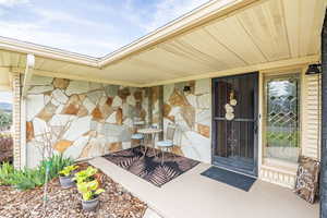 Doorway to property featuring stone siding and covered porch