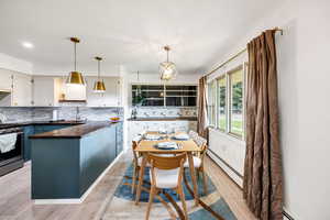 Kitchen with pendant lighting, light wood-style flooring, tasteful backsplash, gas range, and a baseboard radiator