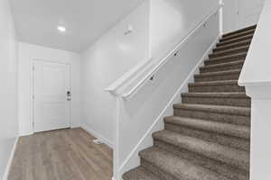 Stairs featuring wood finished floors, baseboards, visible vents, and recessed lighting