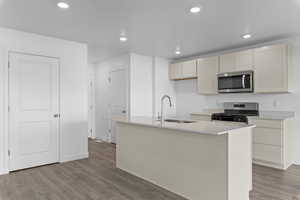 Kitchen with a sink, appliances with stainless steel finishes, a kitchen island with sink, recessed lighting, and light wood-style flooring
