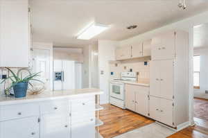Kitchen with backsplash, light countertops, light wood finished floors, and white appliances