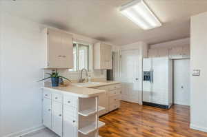 Kitchen with tasteful backsplash, white refrigerator with ice dispenser, open shelves, wood finished floors, and a sink
