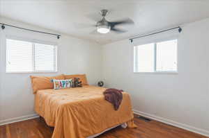 Bedroom with dark wood-style flooring, visible vents, baseboards, and multiple windows