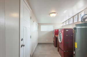 Washroom with washer and dryer, laundry area, baseboards, and water heater