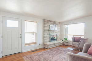 Living room featuring a fireplace, visible vents, baseboards, and wood finished floors