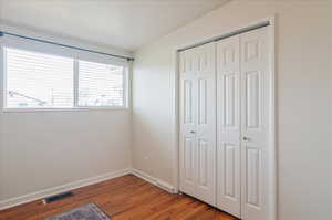 Unfurnished bedroom with visible vents, a closet, baseboards, and wood finished floors