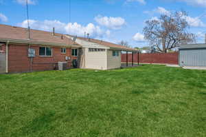 Rear view of property with a shed, central AC, a yard, a fenced backyard, and an outdoor structure