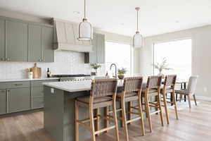 Kitchen with tasteful backsplash, premium range hood, light wood finished floors, and green cabinetry