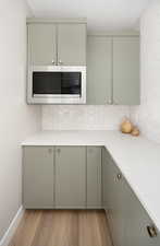 Kitchen with light countertops, stainless steel microwave, gray cabinetry, backsplash, and light wood-style flooring
