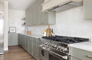 Kitchen with premium appliances, tasteful backsplash, premium range hood, and light countertops