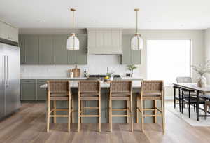 Kitchen featuring custom exhaust hood, light countertops, light wood-style floors, high end refrigerator, and backsplash