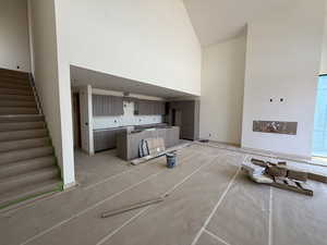 Unfurnished living room featuring high vaulted ceiling and stairs