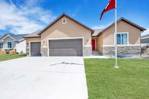 Ranch-style house with a garage, stucco siding, stone siding, and a front lawn