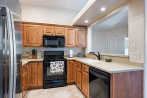Kitchen featuring light tile patterned floors, a sink, light countertops, brown cabinets, and black appliances