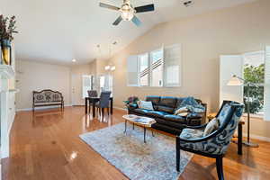 Living area featuring light wood-type flooring, baseboards, visible vents, lofted ceiling, and ceiling fan with notable chandelier
