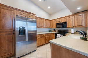 Kitchen with light countertops, light tile patterned floors, a sink, and black appliances