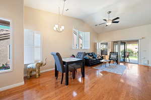 Dining space featuring light wood-type flooring, ceiling fan with notable chandelier, baseboards, and lofted ceiling