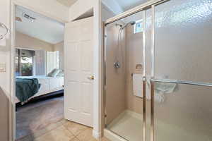 Ensuite bathroom featuring connected bathroom, tile patterned flooring, visible vents, lofted ceiling, and a stall shower