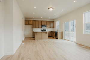 Kitchen featuring light wood-type flooring, a center island, baseboards, and stainless steel appliances