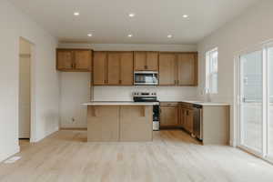 Kitchen featuring light wood-type flooring, visible vents, brown cabinetry, light countertops, and appliances with stainless steel finishes