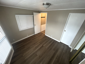 Unfurnished bedroom with dark wood-type flooring, baseboards, ornamental molding, and a textured ceiling