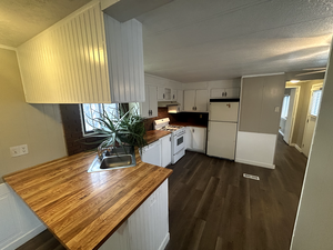 Kitchen featuring a sink, under cabinet range hood, white appliances, and dark wood-style floors