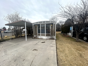 Back of house featuring a yard, a carport, a sunroom, and driveway