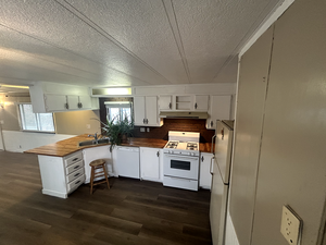 Kitchen featuring range hood, white appliances, butcher block countertops, and dark wood-style floors