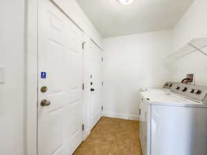 Clothes washing area featuring washer and dryer, laundry area, light tile patterned floors, and baseboards