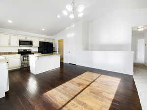Kitchen featuring vaulted ceiling, light stone counters, a center island, dark wood finished floors, and appliances with stainless steel finishes