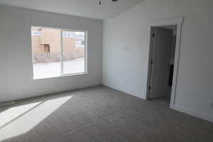 Carpeted spare room featuring visible vents, baseboards, a ceiling fan, and vaulted ceiling