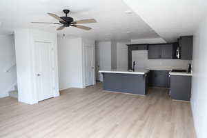 Kitchen featuring ceiling fan, light wood-type flooring, a kitchen island with sink, light countertops, and baseboards