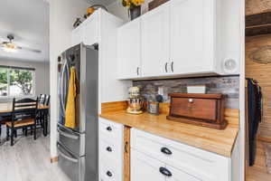 Kitchen with white cabinets, light wood-type flooring, freestanding refrigerator, and wooden counters