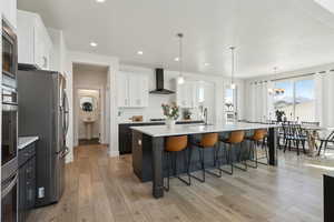 Kitchen with a breakfast bar, wall chimney range hood, light countertops, white cabinetry, and appliances with stainless steel finishes