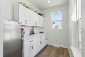 Interior space featuring visible vents, baseboards, stainless steel fridge, light wood-type flooring, and recessed lighting