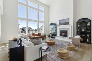 Living room with light wood-type flooring, a towering ceiling, and a glass covered fireplace