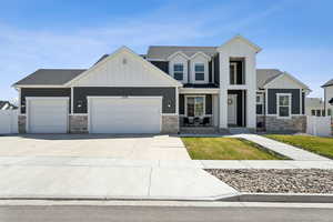 View of front of house featuring an attached garage, board and batten siding, fence, and stone siding