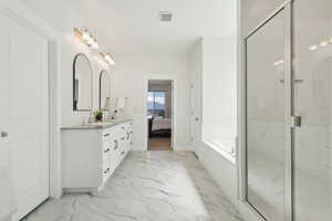Ensuite bathroom featuring double vanity, marble finish floor, a sink, and a garden tub