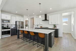 Kitchen featuring light countertops, wall chimney exhaust hood, a breakfast bar area, appliances with stainless steel finishes, and a sink