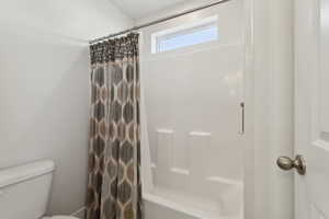 Bathroom with shower / bathtub combination with curtain and toilet