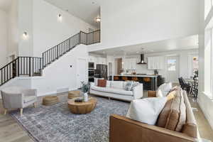 Living room with a towering ceiling, baseboards, stairs, light wood-style floors, and visible vents