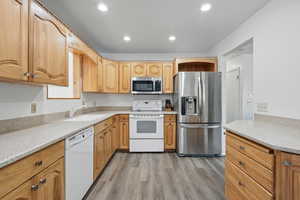 Kitchen featuring light wood-type flooring, recessed lighting, light countertops, appliances with stainless steel finishes, and a sink