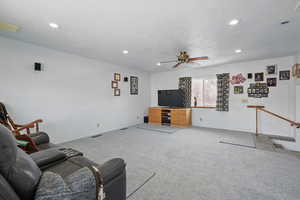 Carpeted living room with ceiling fan, baseboards, visible vents, and recessed lighting