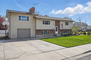 Bi-level home with a chimney, driveway, a front lawn, brick siding, and a garage