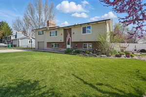 Split foyer home featuring a front yard, a garage, a chimney, fence, and driveway