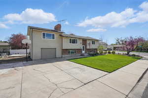 Bi-level home with fence, a front lawn, an attached garage, a chimney, and driveway