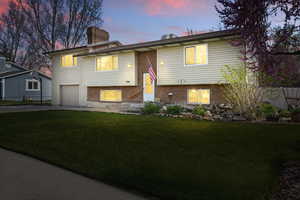 Raised ranch featuring an attached garage, a chimney, brick siding, a front lawn, and driveway